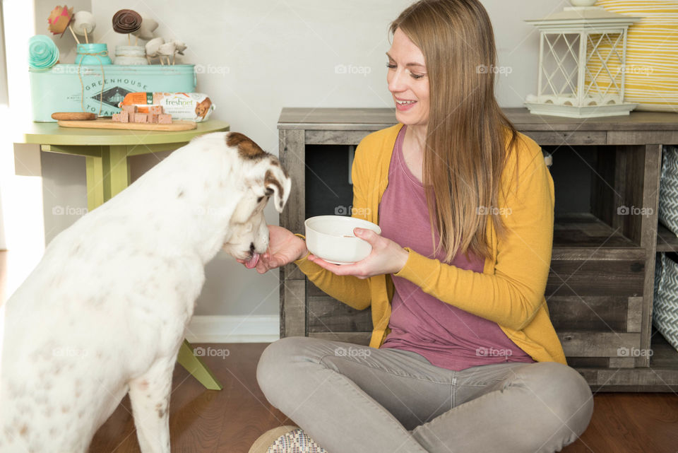 Young woman sitting on the floor and feeding her dog