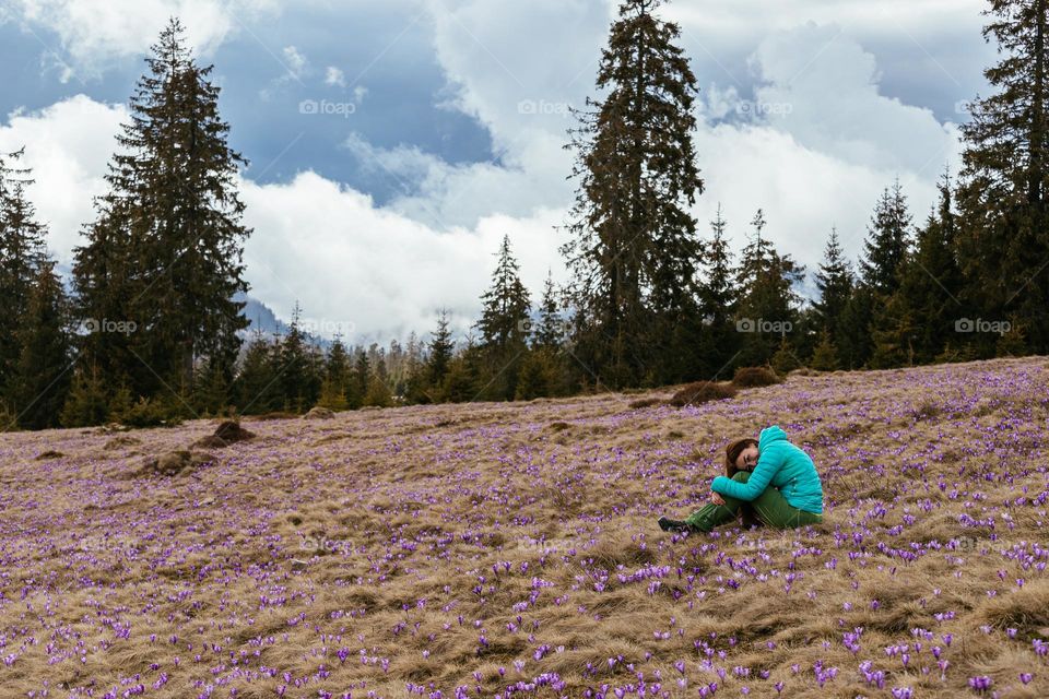 Woman while on a hike in the mountains, laying in a meadow full of spring crocus flowers.