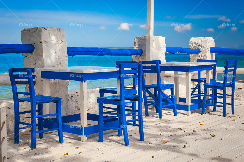 Tavern outdoor white and blue tables and chairs next to sea.