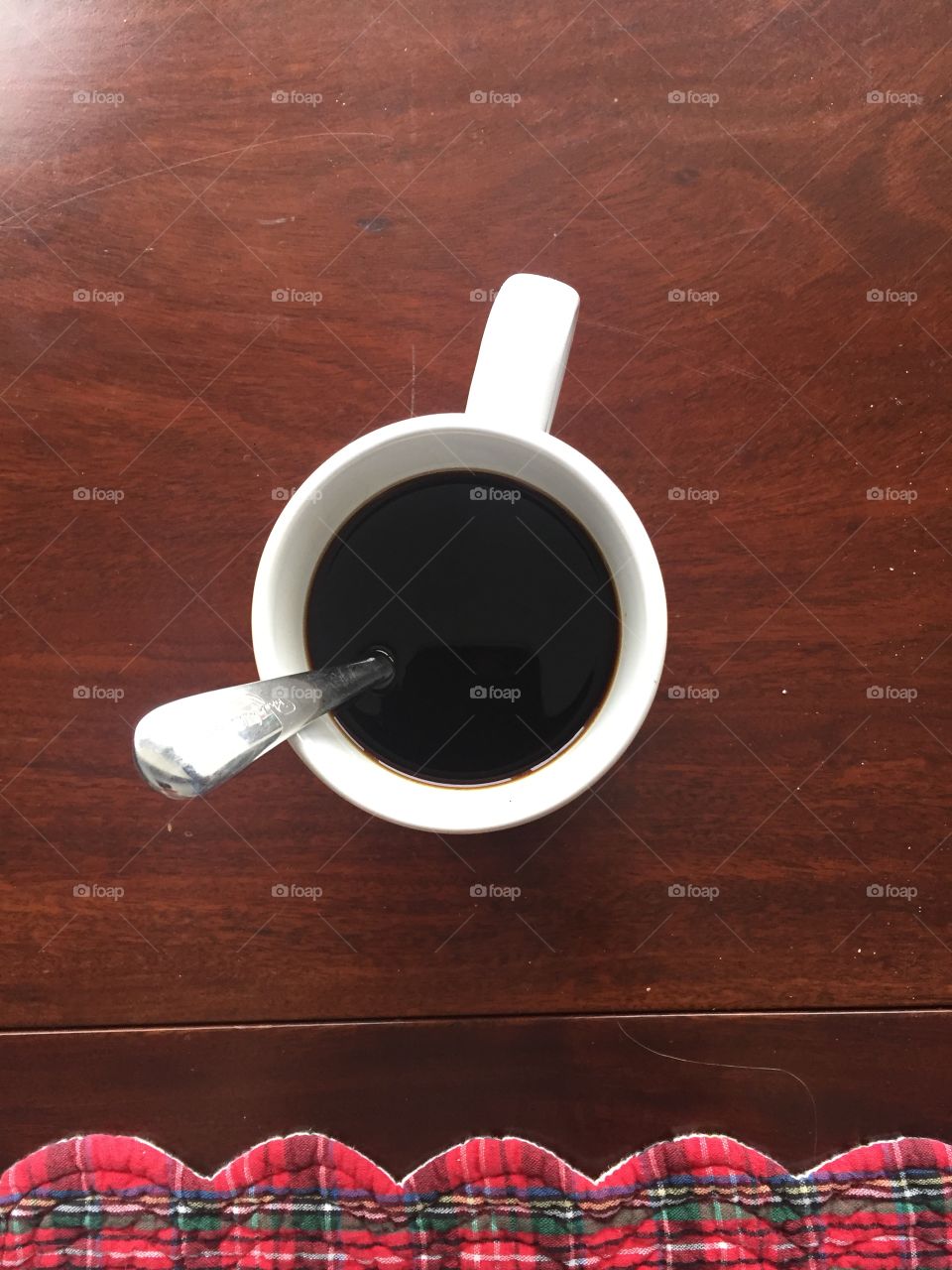 A fresh cup of black coffee as seen from above. The coffee is in a white cup and a silver spoon sits in it at an angle.