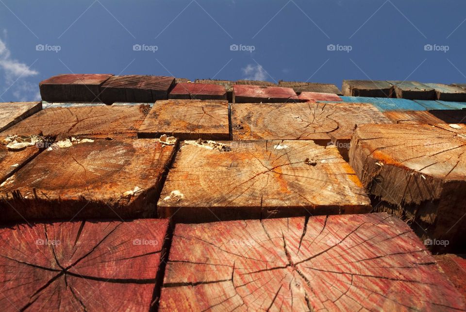 A stock pile of timber and wooden logs are seen from a low angle perspective with blue skies in the background.