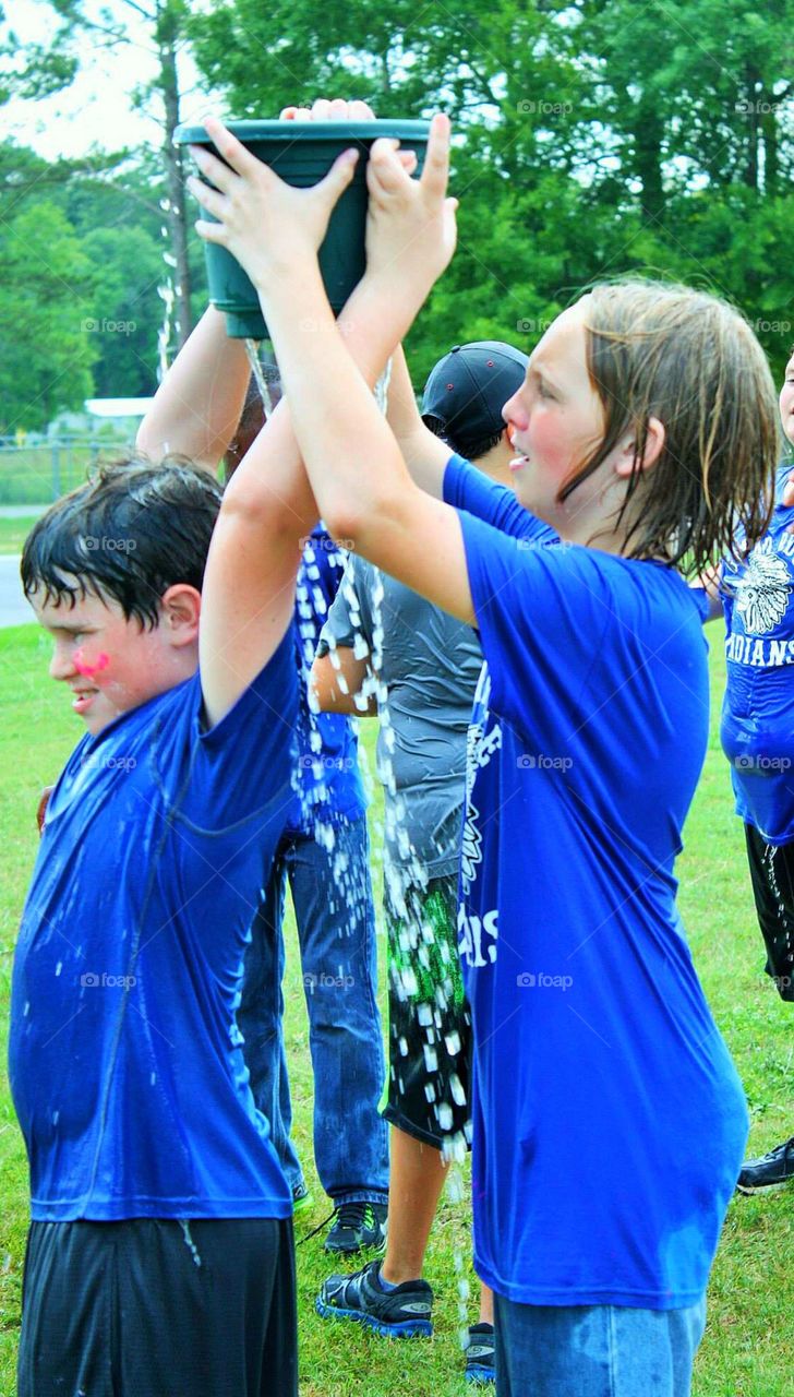 Girl and boy holding water bucket over head