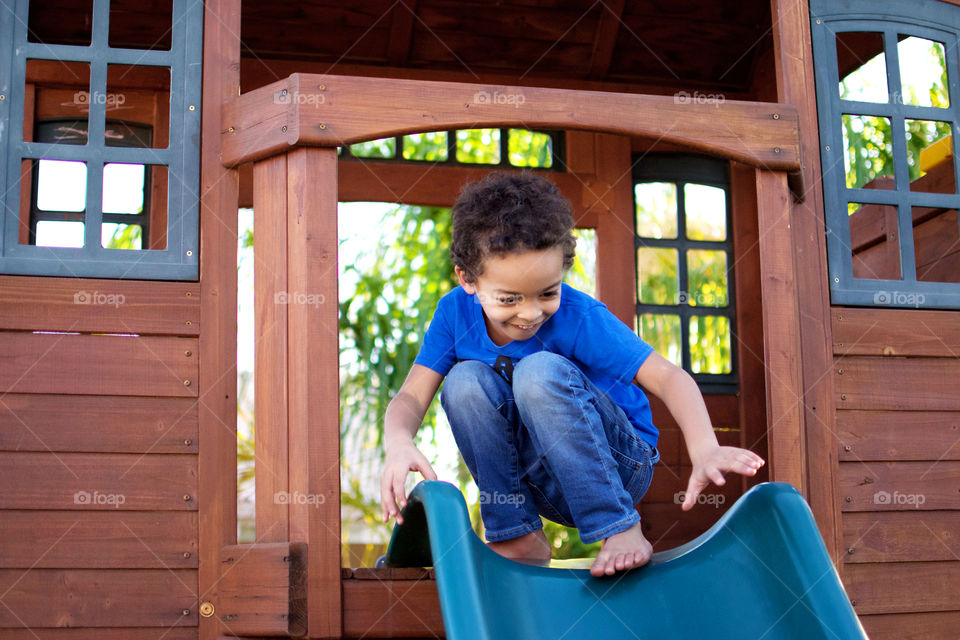 Biracial boy surfing down slide