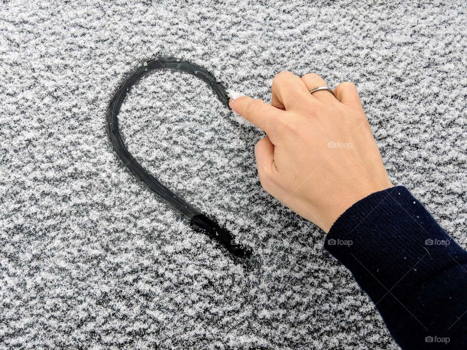 hand drawing a heart on a snowy window