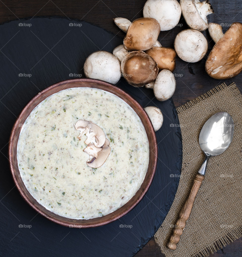 Mushroom cream soup in brown bowl with ingredients on dark background