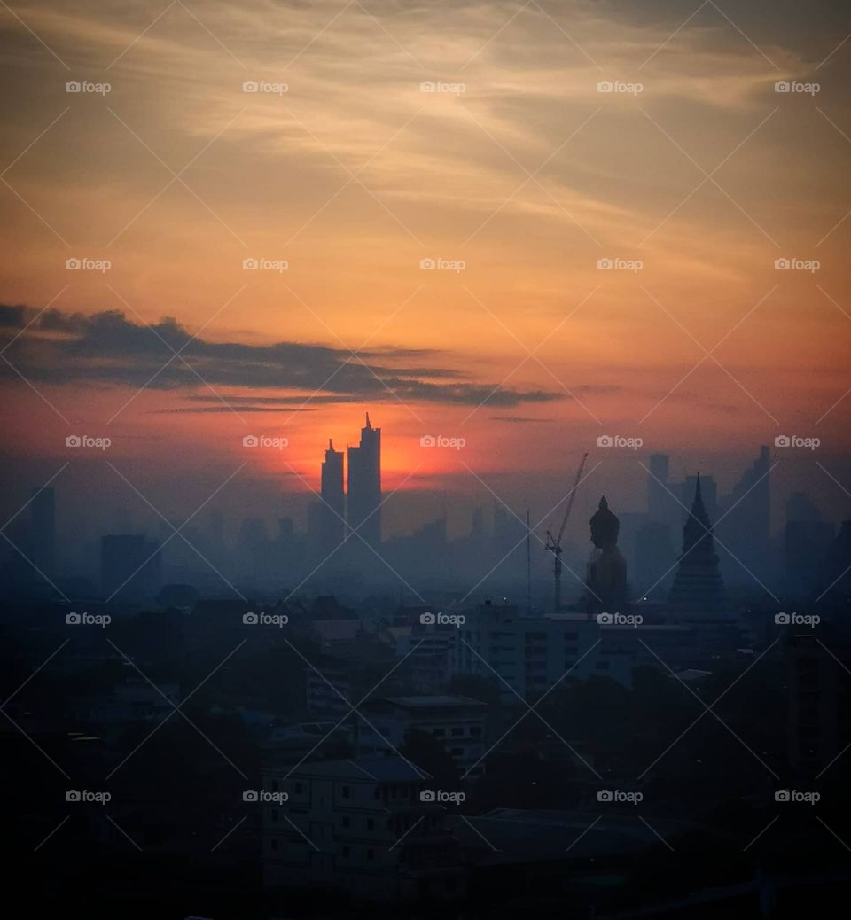 The sun rises over Bangkok. The silhouette of Wat Paknam sits in front of the skyline.