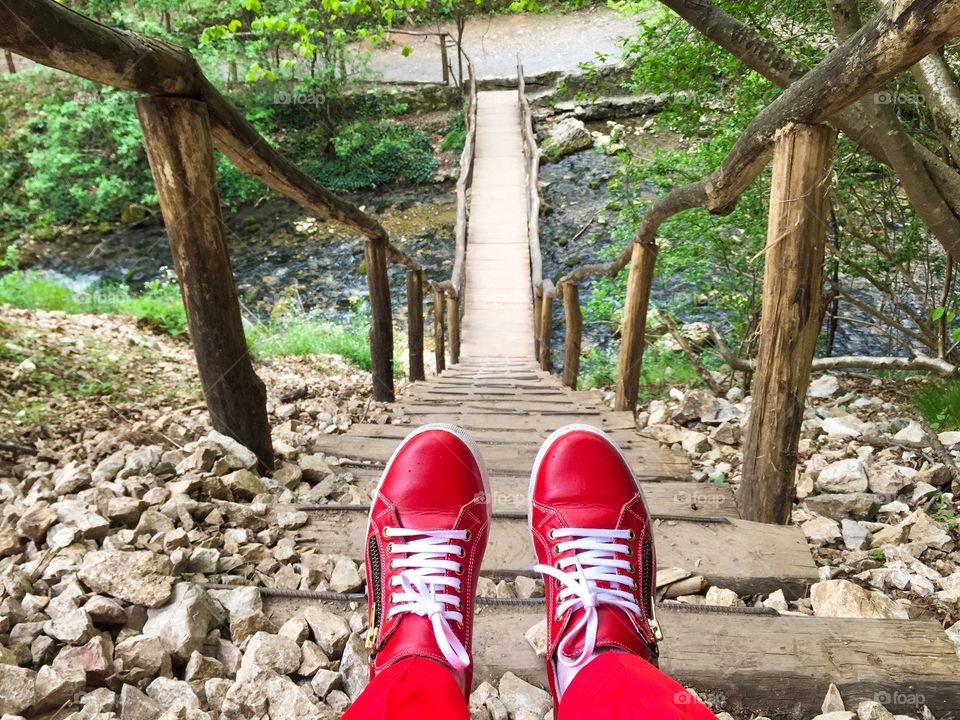 Women red sneakers with white laces on the steps of a wooden bridge