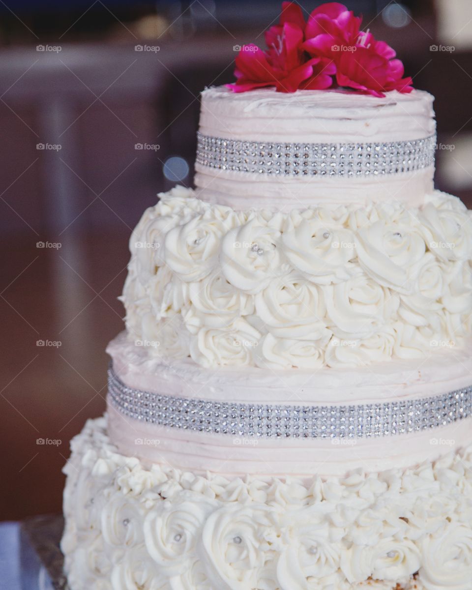 A fancy cake with massive pink flowers and decorated with glitter and white flowers