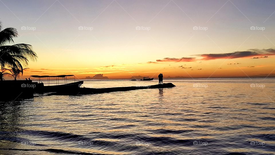 Una pareja observando la puesta del sol sobre un pequeño atracadero en el mar. Utila, Islas de la Bahia.