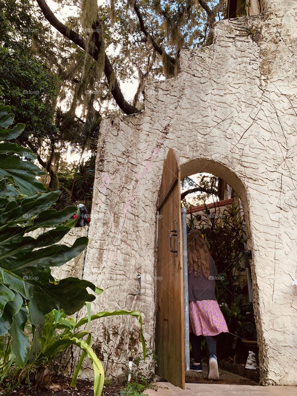 White and red spanish old style architecture residential large house built in the early 1900s. Doorway with antique style wood door in a stairway wall seen from tropical plants with a young girl walking inside the other side.