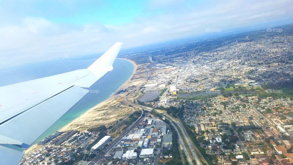 Flying over city in a plane with visible buildings highway and ocean coast