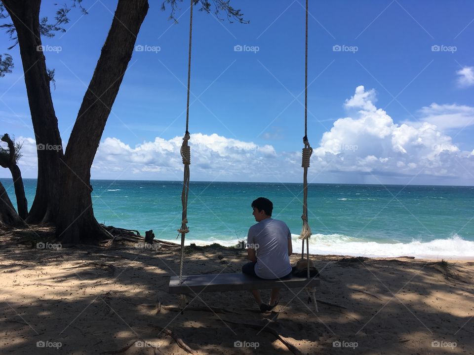 Man sitting blissfully on tree swing overlooking a blue sea