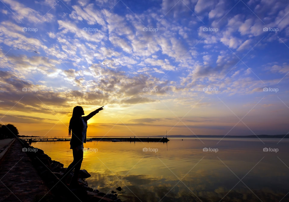 Silhouette of female person enjoying sunset and view by lake 