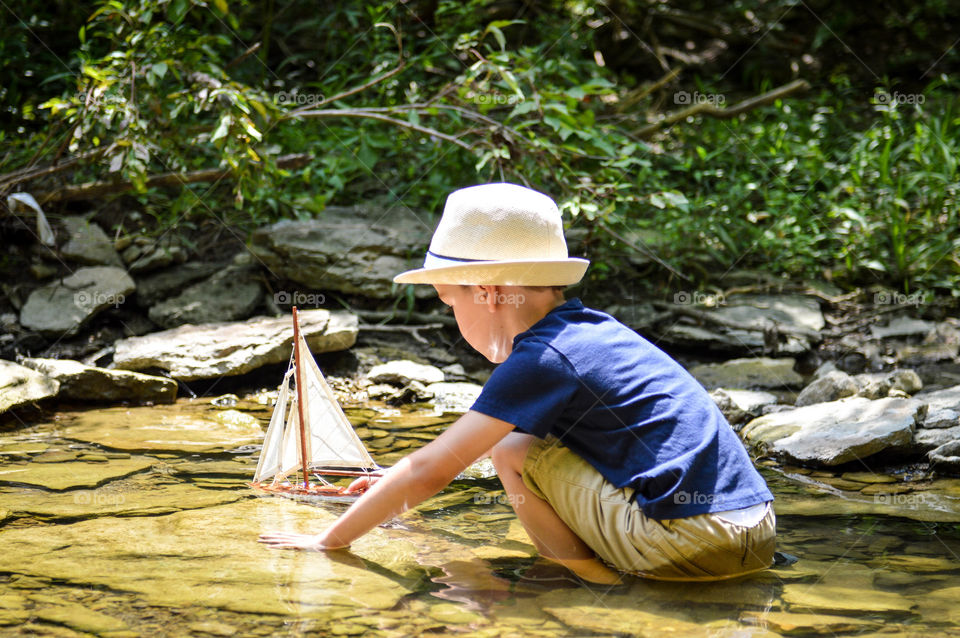 Young boy playing with a toy sailboat in a creek 