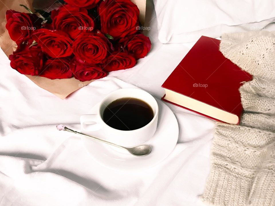 Coffee, book, roses and knitted sweater in bed 