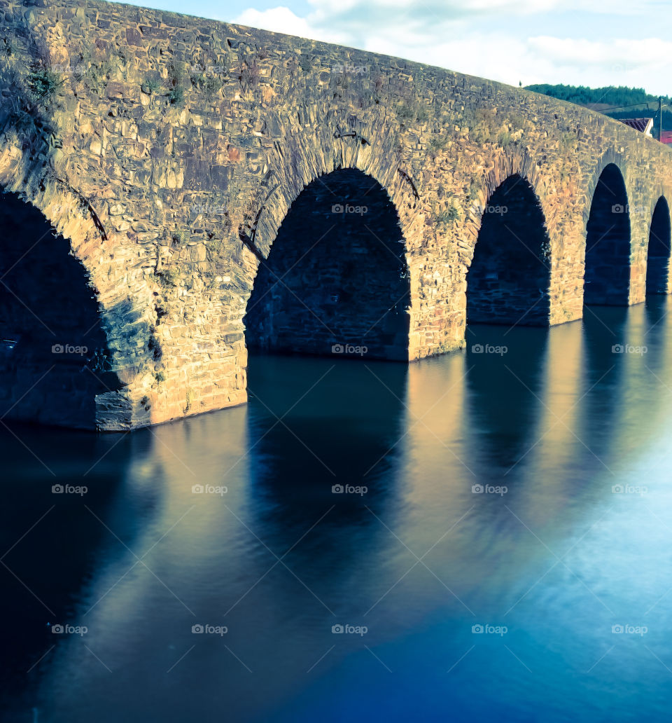 The reflection of a stone arched bridge create circular patterns with the water