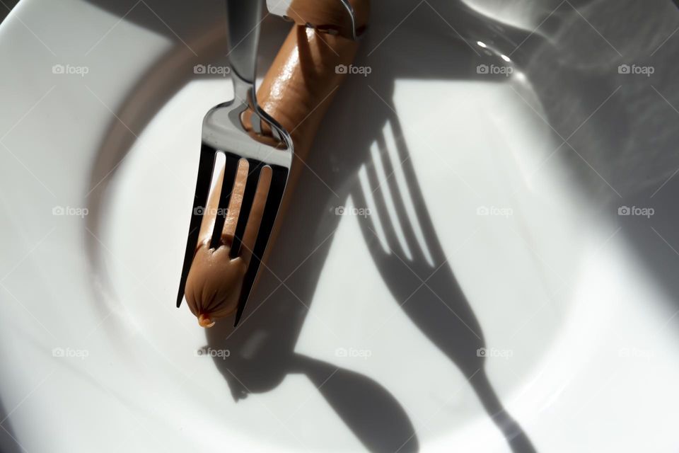 One sausage and two forks on a white porcelain plate.