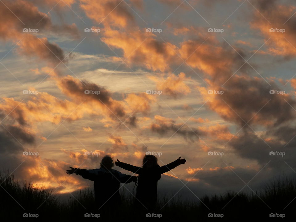 Silhouette of Best Friends On A Hill Embracing A Beautiful Sunset Sky With Hands In The Air - Celebration