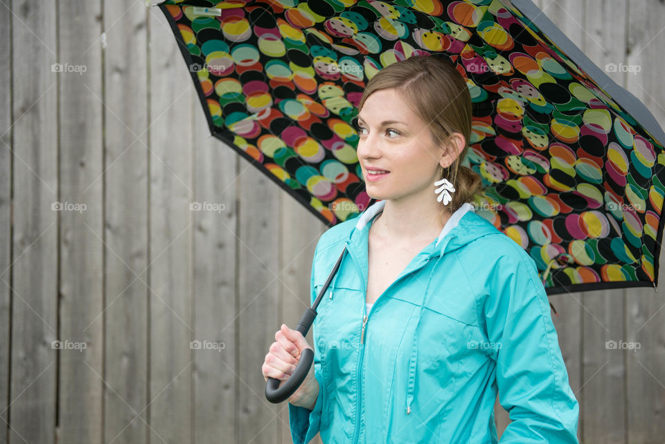 Young woman wearing a raincoat and smiling while holding an umbrella