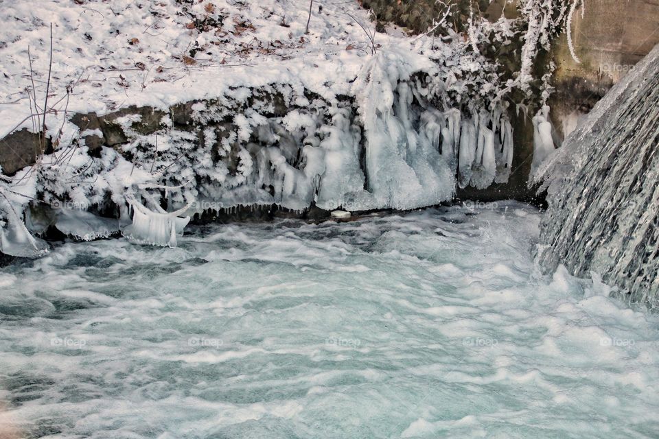 Icicles and bizarre formed ice sculptures hang from branches and grass in a stream