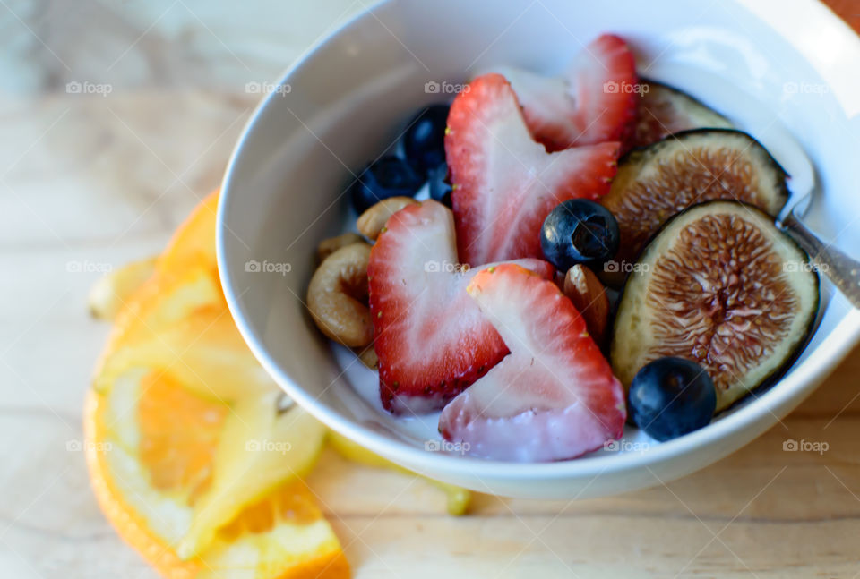 Fresh smoothie bowl topped with heart shaped strawberries, fig, blueberries, cashew nuts and almonds with honey closeup healthy lifestyle food photography 