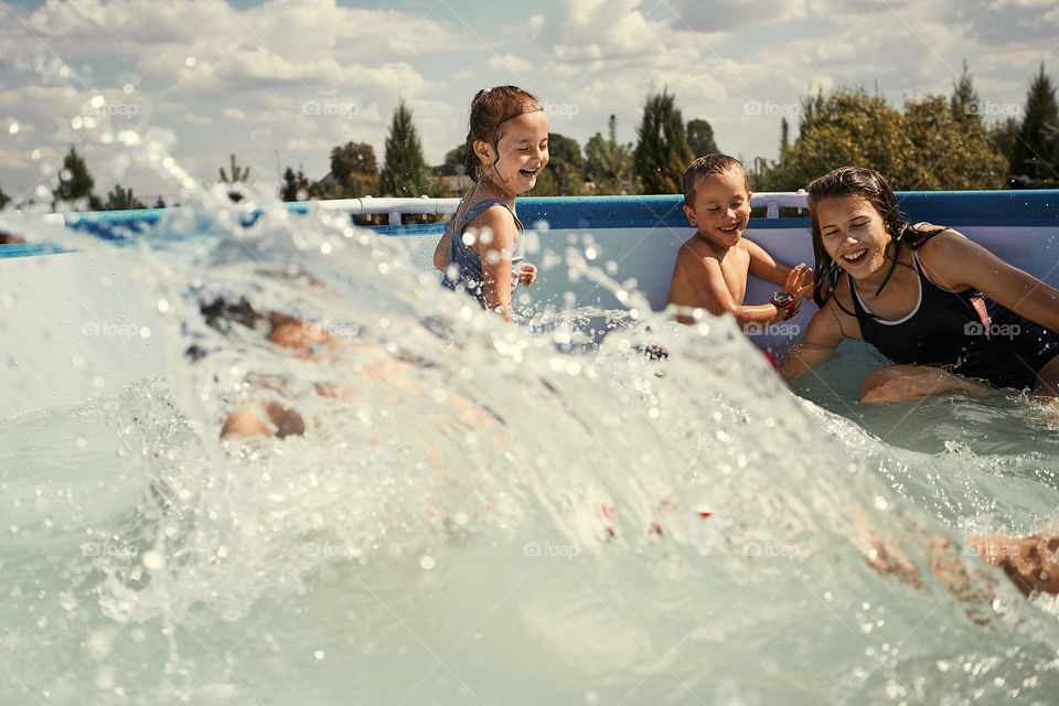 Children splashing, jumping, playing in a pool in backyard on summer vacation day. Real people, authentic situations