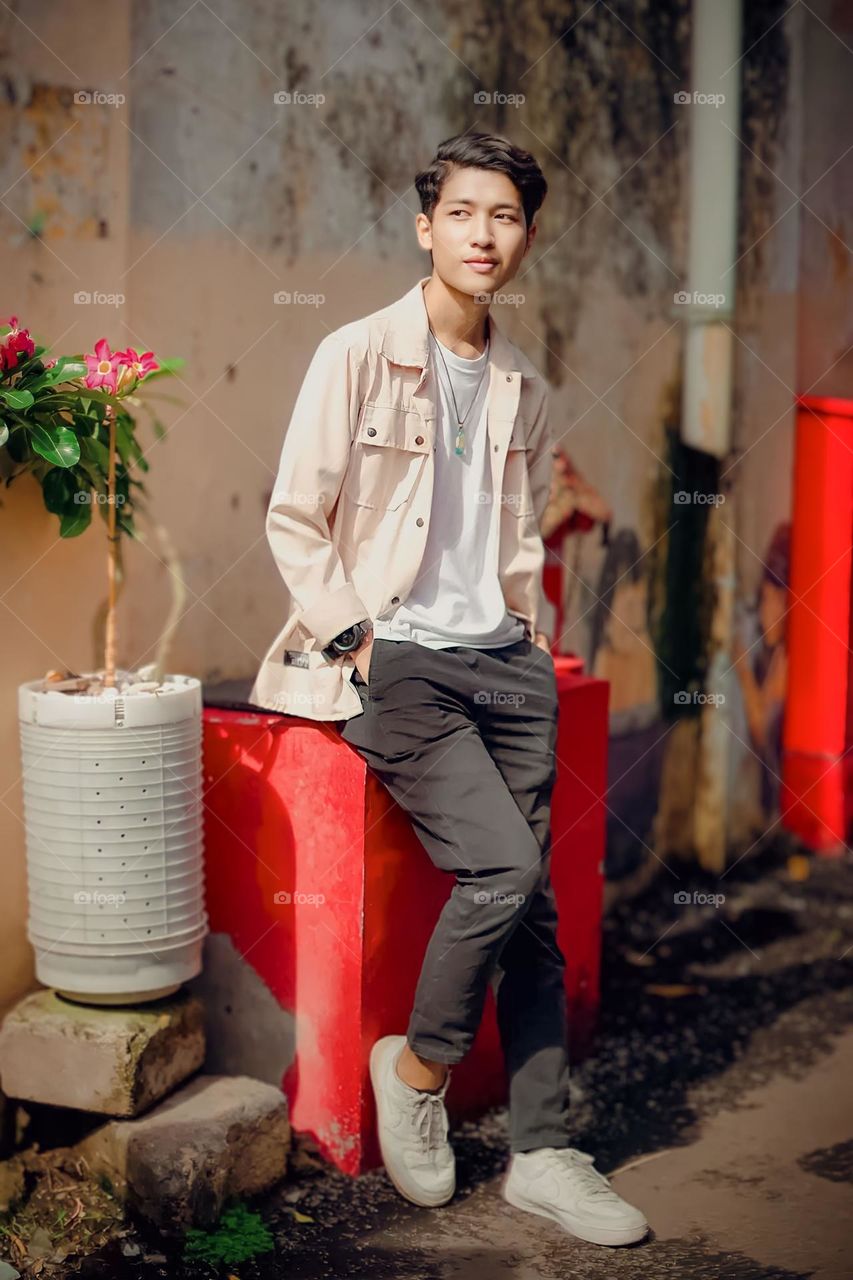 Portrait of a young man sitting on a large red object near a worn wall