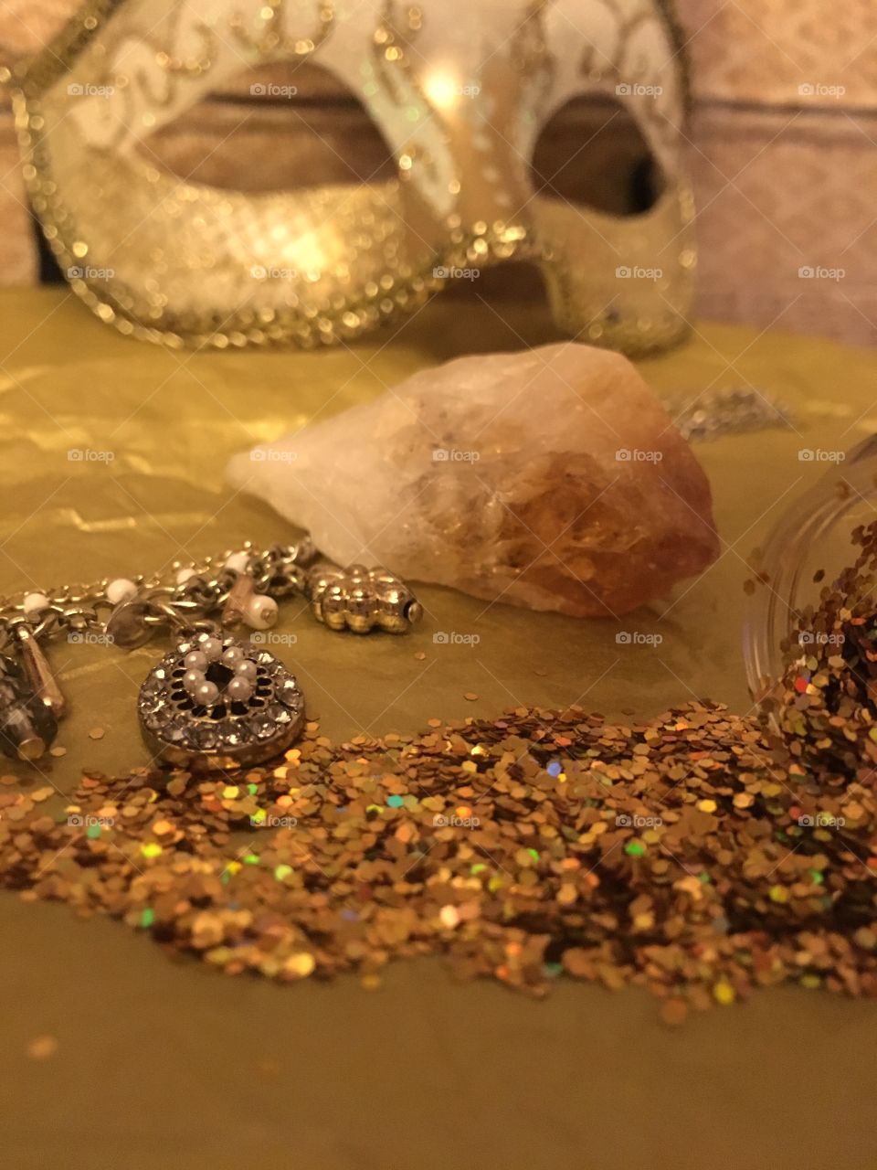 Gold glitter spilled on a table with gold charm necklace and citrine rock crystal and masquerade mask 