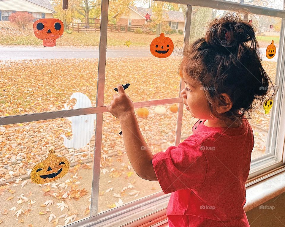 Toddler girl playing with Halloween decorations, toddler girl helps to decorate house for Halloween, Halloween decor, ready for trick or treaters, ready for Halloween, decorate the windows, child helps with decorations for Halloween