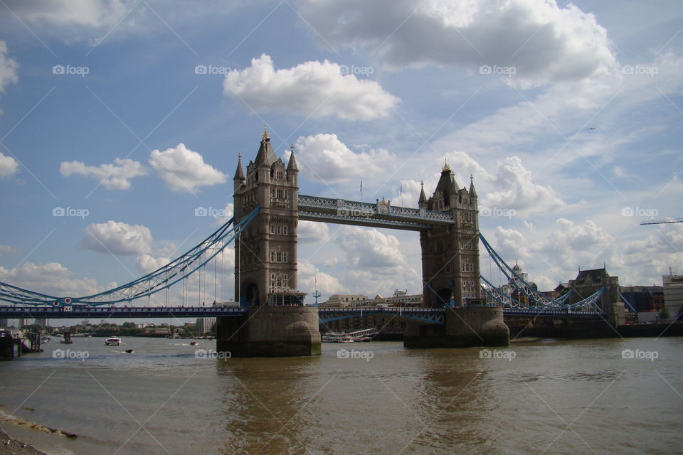 London tower bridge from a short distance, against a bright blue sky with fluffy white clouds.