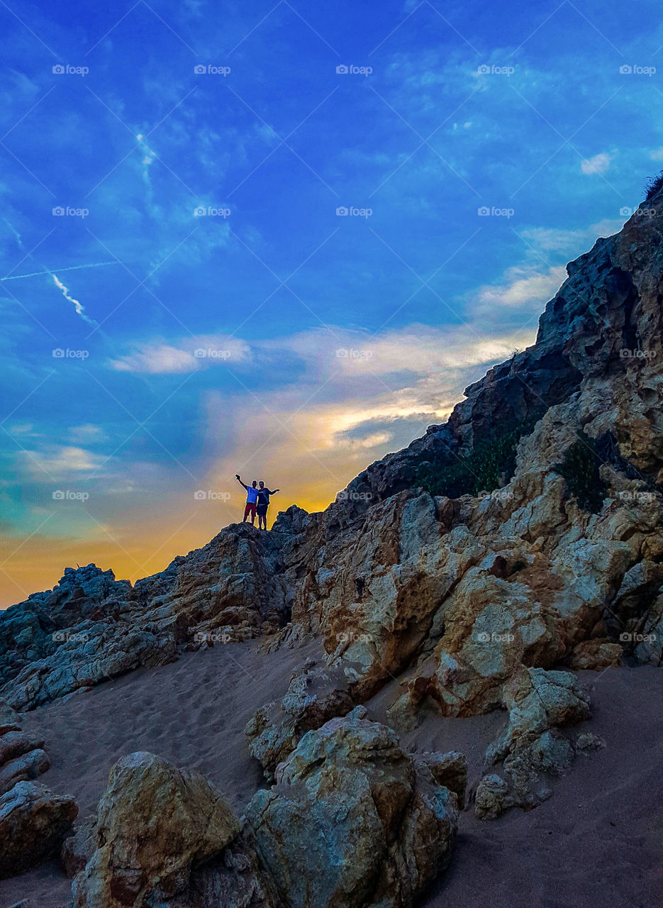 two people standing on rocks against dramatic sky