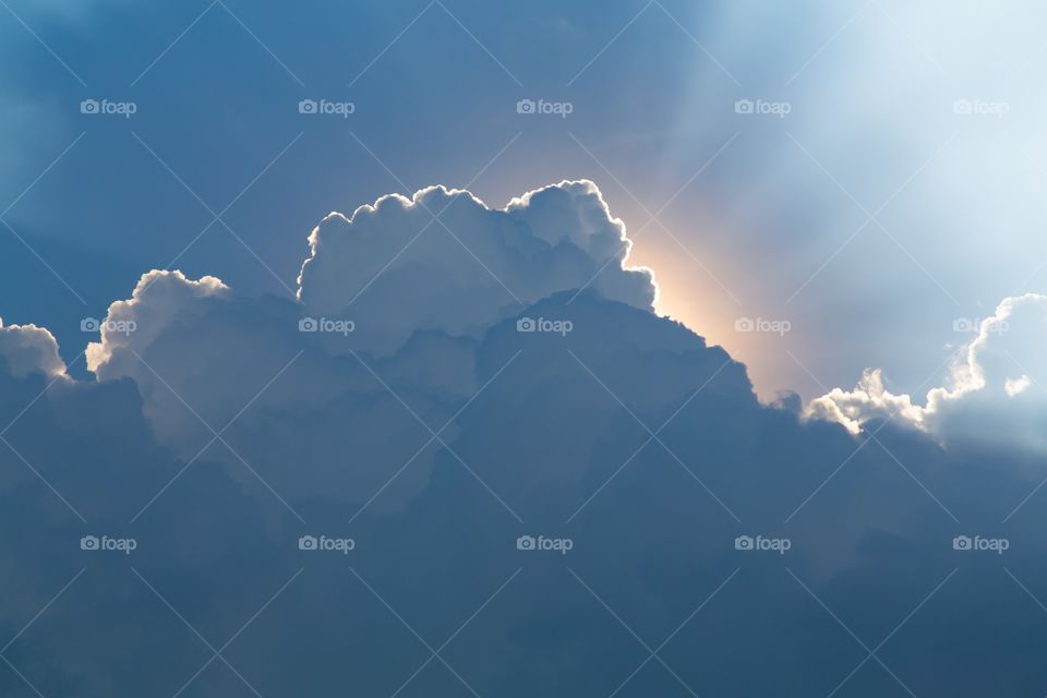 Sun behind clouds. Clear sky on the top and storm clouds on the bottom. Sun behind the clouds forming white God Rays