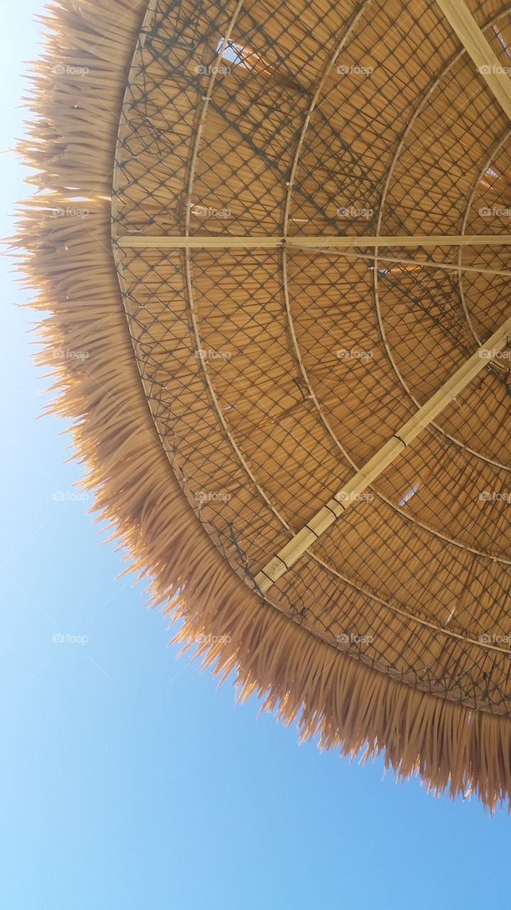 Low angle view of a straw beach umbrella against a blue sky at Hawaii