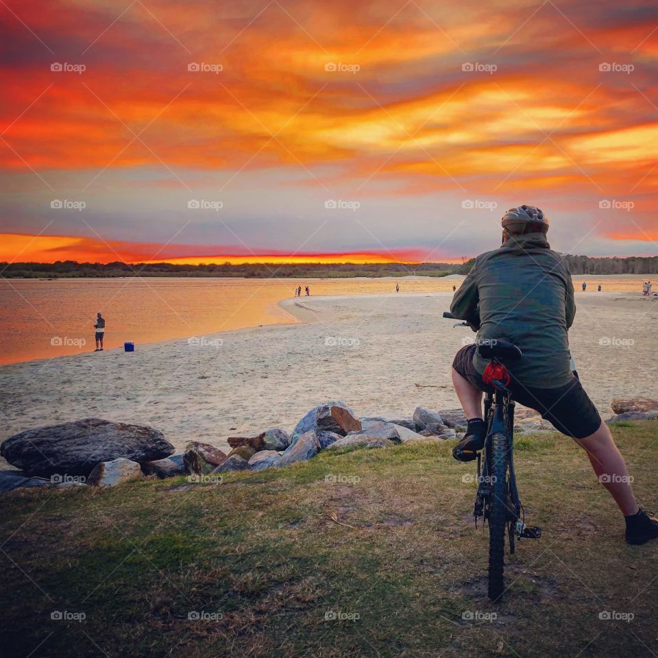 Blazing red orange sunset at the beach watched by a cyclist 