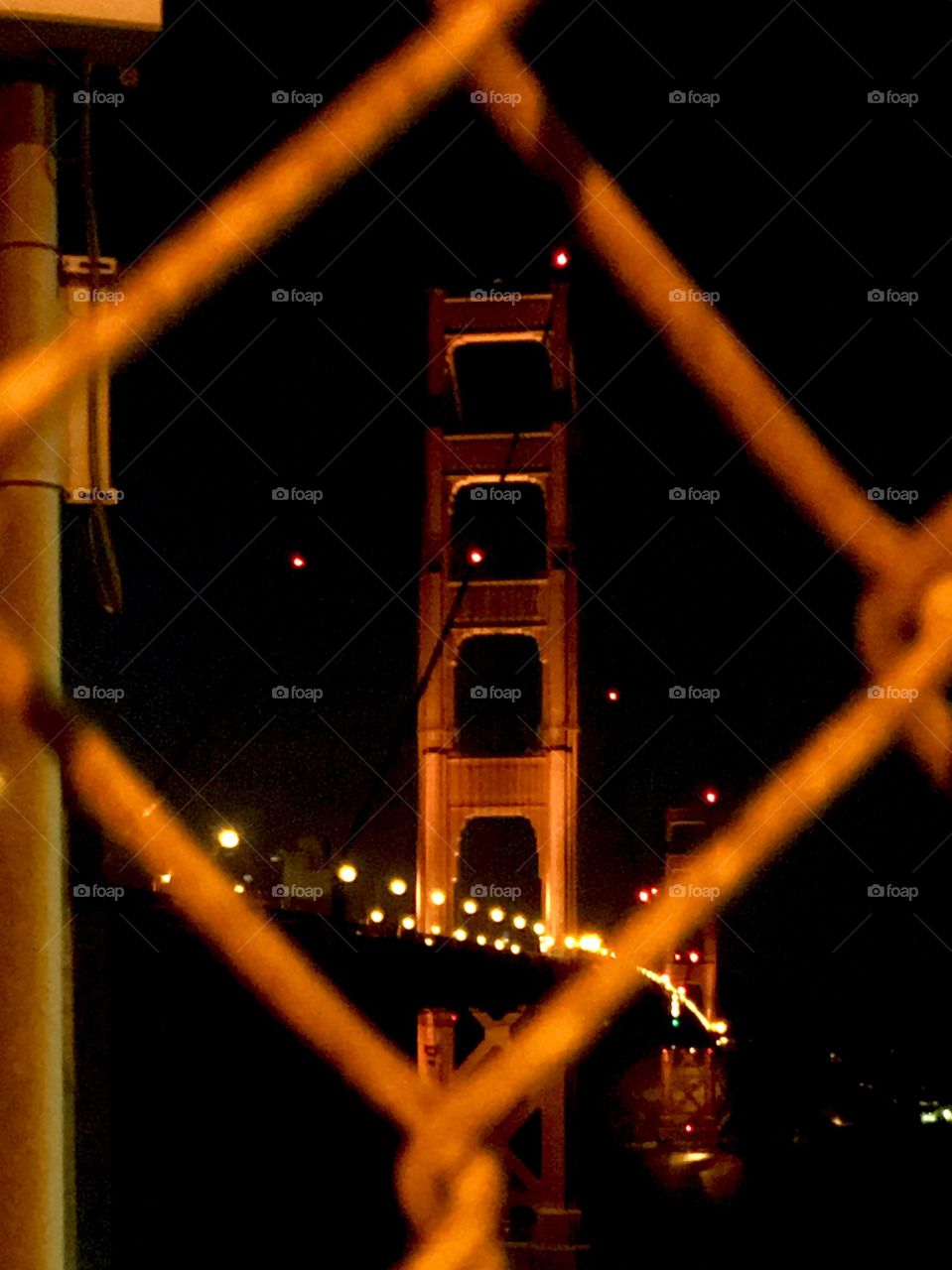 Golden Gate Bridge at night. Seen through a chain link fence. 