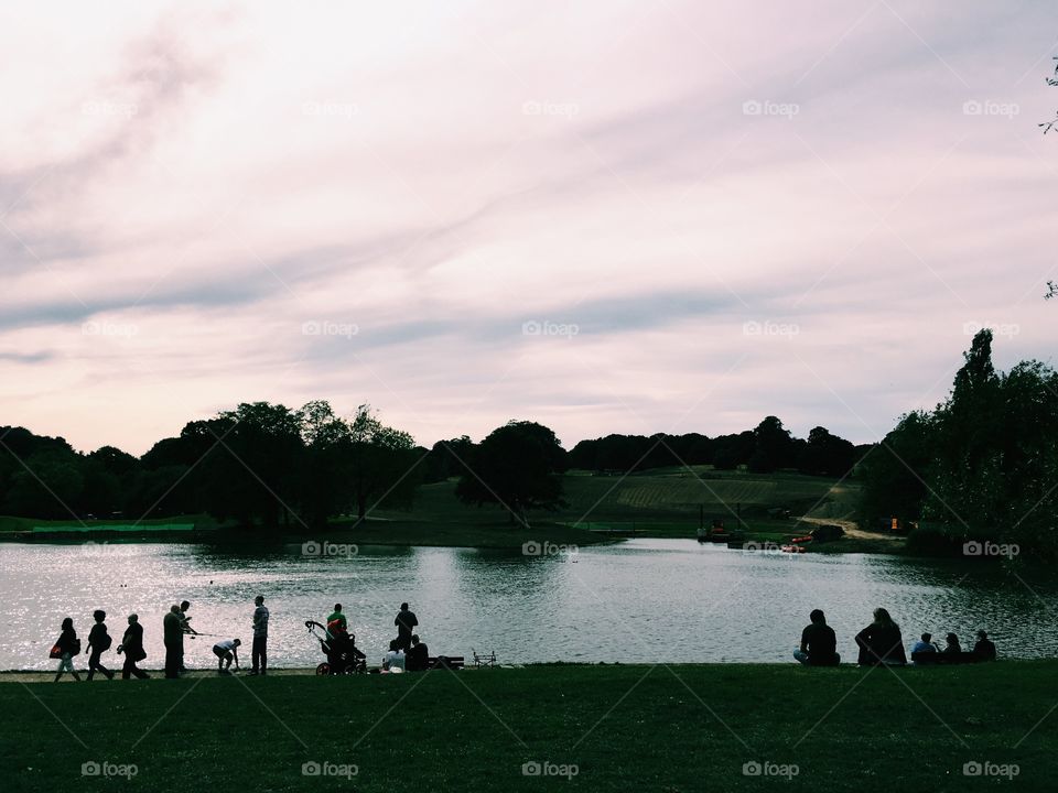 Silhouette of people walking by a pond in Hampstead Heath park in London England