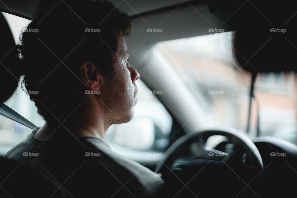 Portrait of a young Caucasian man driving a car and looking intently at the road, close-up view from the side. The concept of a road trip.