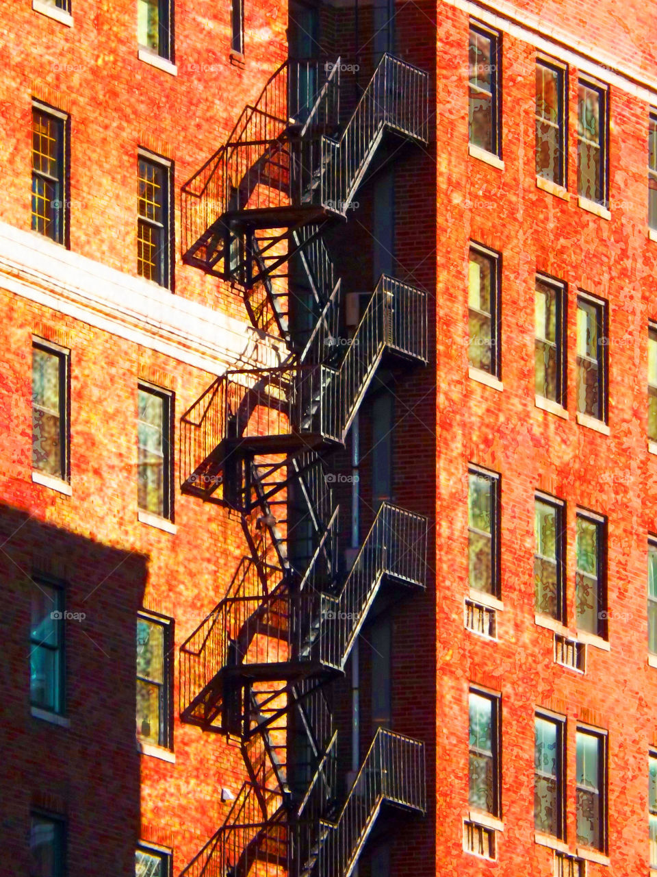 Tall Building with Fire Escape. Two buildings stand side by side with a fire escape going up one side of the building on the right. For a moment it almost looks like an optical illusion.