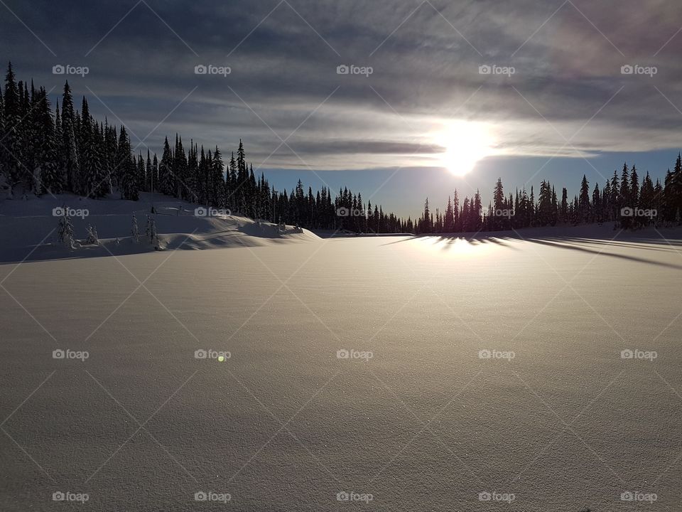 Sun peeking out from beneath the clouds over a snow covered lake