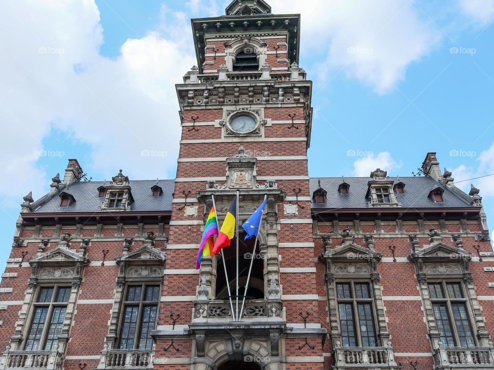 Beautiful view of Anderlecht district commune building with three developing LGBT flags in the middle on a summer sunny day with a clear blue sky with big white clouds,close-up view from below.