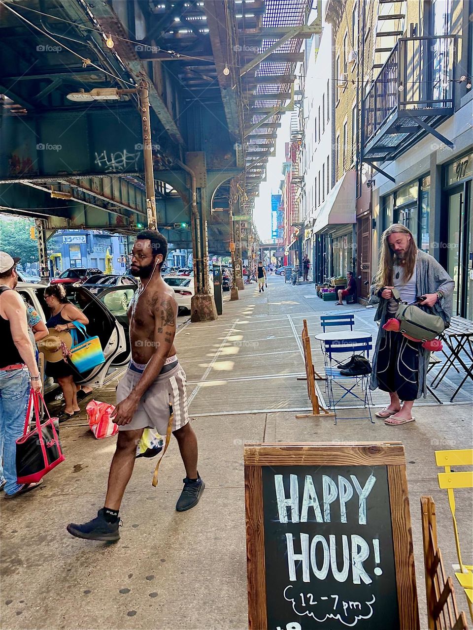 At “HAPPY HOUR” the people on “Broadway” and “Myrtle Ave” under the “M” train overpass at the “Myrtle Ave” station rejoice getting ready to frequent the bar for half price drinks. 2024. Hypnotic Productions