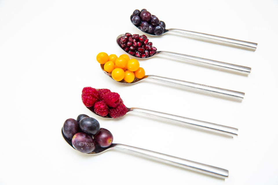 Fresh fruit on symmetrical silver spoons on a white background