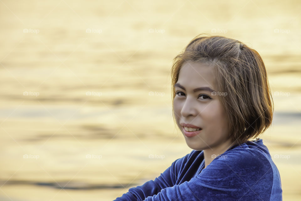 Portrait of Asian woman sitting by the river and the reflected light gold in water.