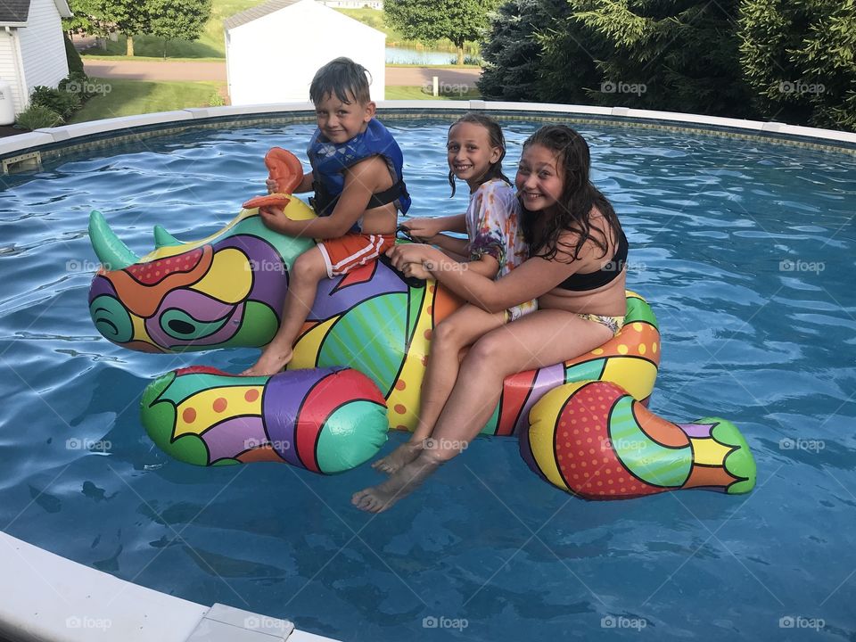 My three kiddos riding on a giant colorful inflatable rhino float in our pool. Water fun! 
