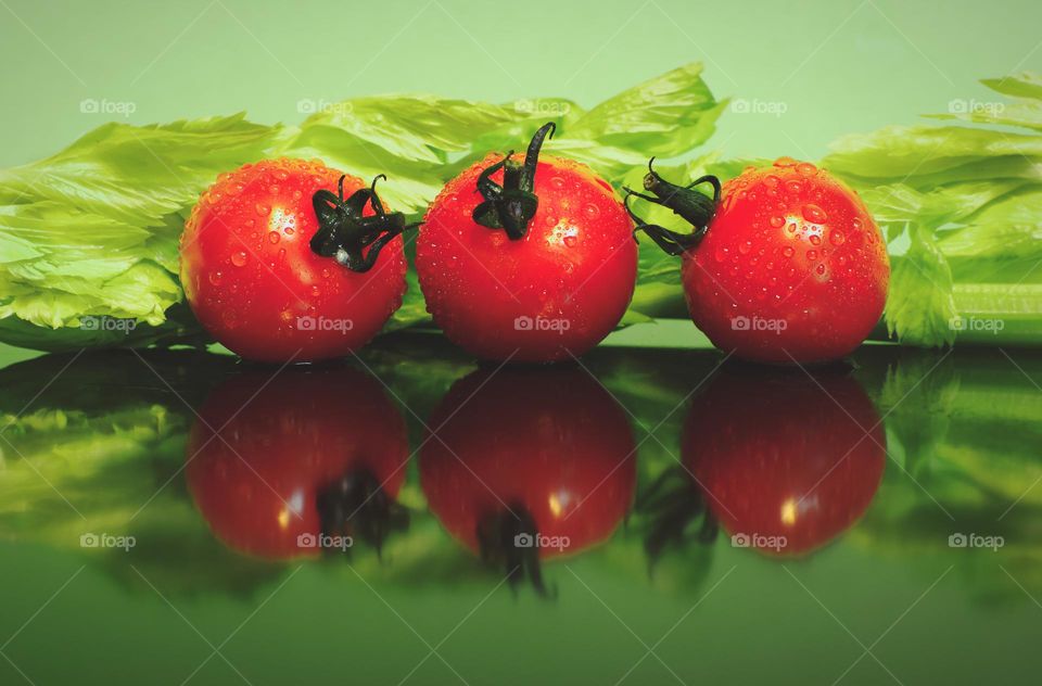 Tomatoes reflected in glass surface with green celery in the background