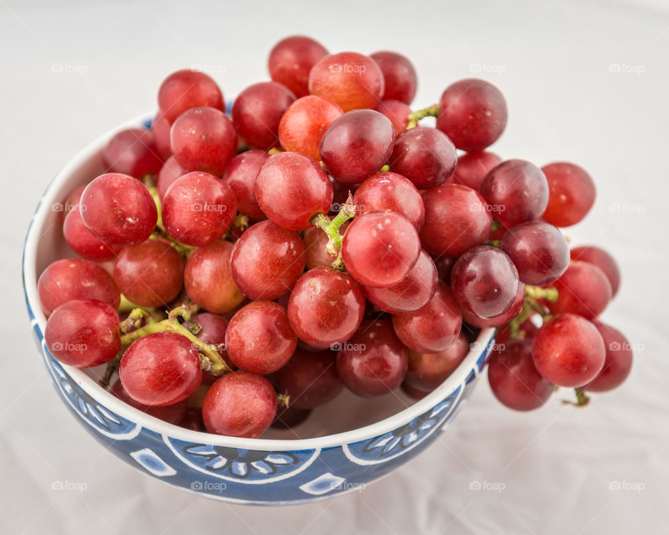 Ceramic bowl full of red grapes. Healthy red grapes in a ceramic bowl on the white table