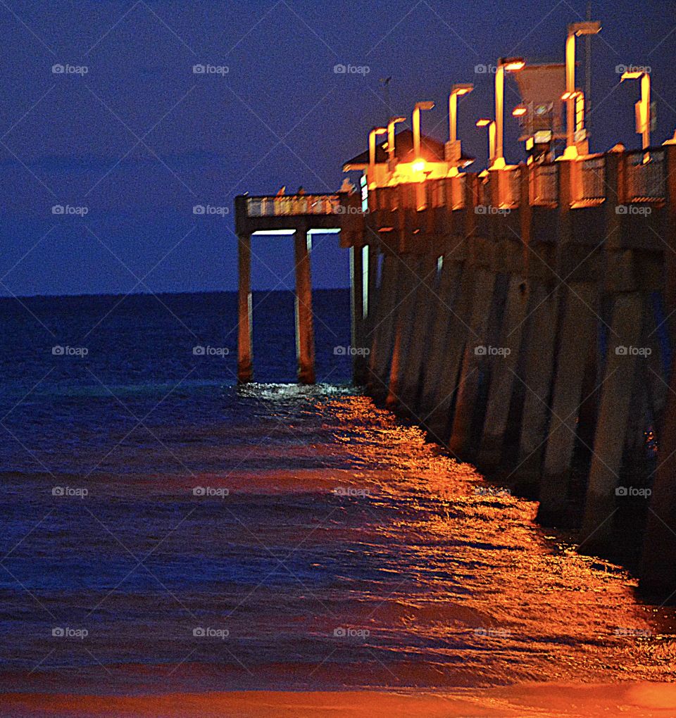 Beauty of the night - Lighted fishing pier reflects light onto the oceans surface
