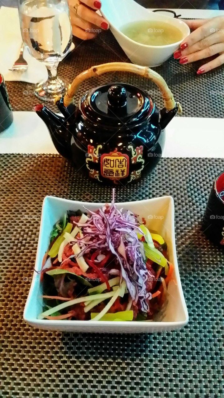 Nice colored asian salad and a bol of soup  with a tea pot and cup