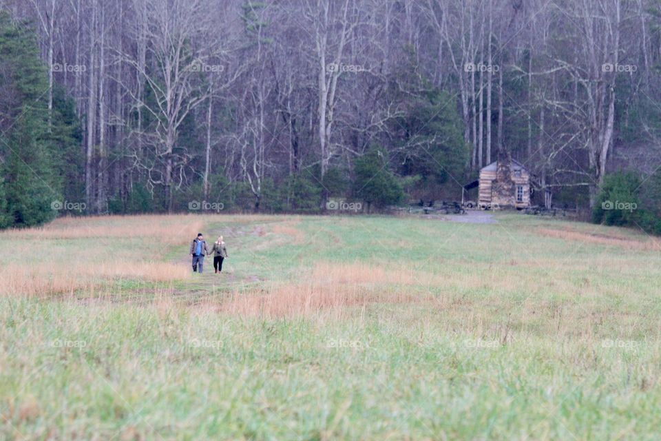 Couple walking through field near log cabin