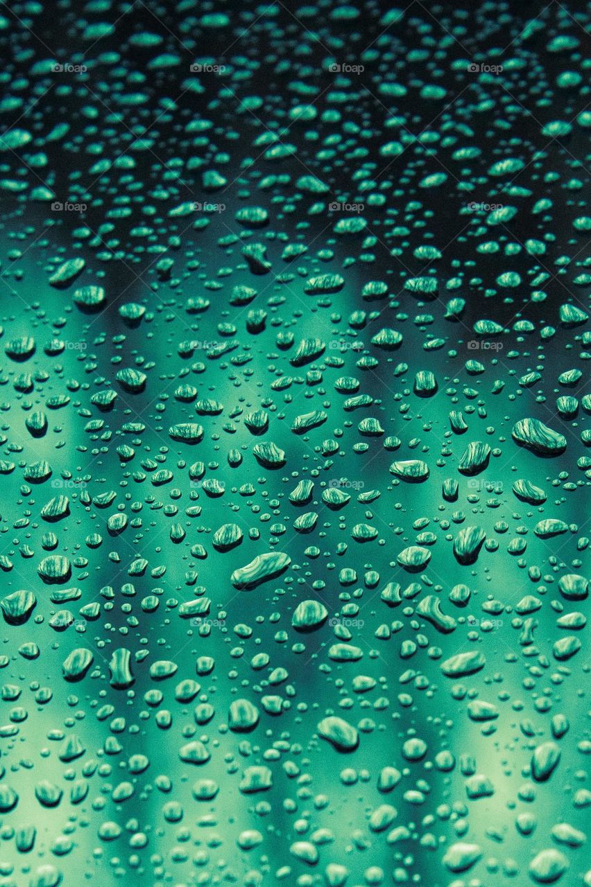 Green reflections in the raindrops. Lots of tiny raindrops on clear glass tinted different hues of green.